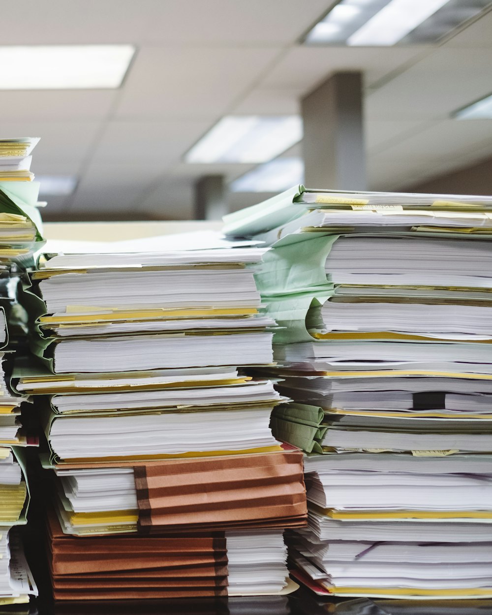 Stacks of paper files and folders piled on office desks